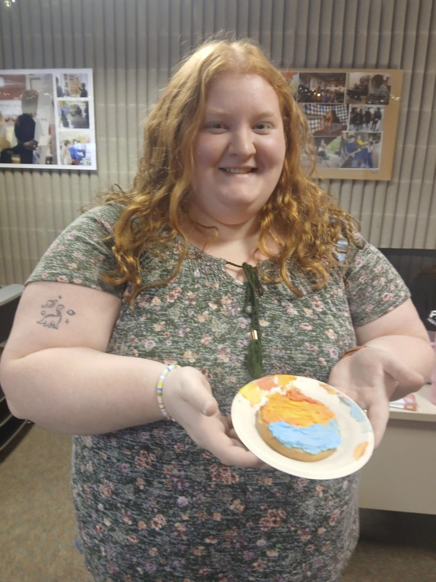 Emaleigh Brooks holds a red, orange, and blue cookie on a plate in the CAB office in the Kelley Center.