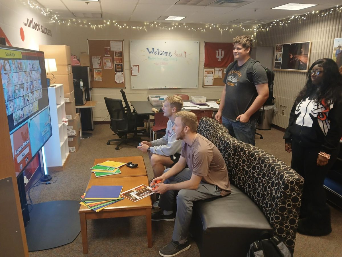 Cody Kretz and Charlie Conkle sit on a couch and play Super Smash Bros on the Nintendo Switch while Farah Harvey and Kayden Pax watch from behind the couch.