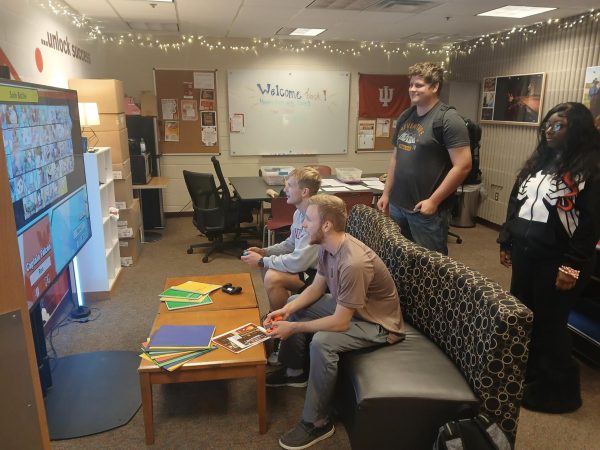 Cody Kretz and Charlie Conkle sit on a couch and play Super Smash Bros on the Nintendo Switch while Farah Harvey and Kayden Pax watch from behind the couch.